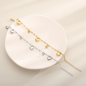 Detail of gold and silver stainless steel anklets with heart charms and beads on white plate