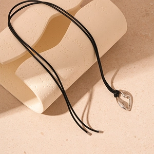 Detailed macro view of irregular heart-shaped hollow silver pendant on black wax cord