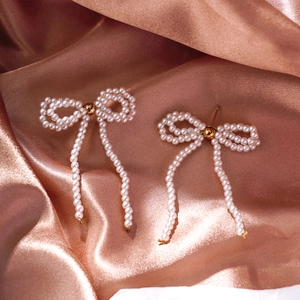 Detail of bow earrings with woven pearls and long tassels on rose gold silk fabric