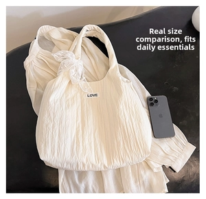 Detail of white pleated tote bag with lace bow and LOVE patch showing size comparison