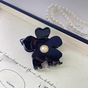 Close-up of a black acetate flower hair claw clip with a faux pearl center on fabric