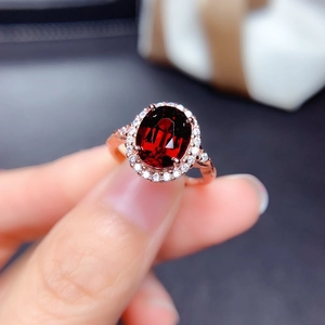 Close-up of an oval-cut dark red garnet ring with a rose gold halo setting on finger