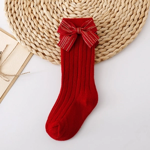 Detail of red knit baby sock with a large gold-striped bow on a white and rustic background