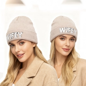 Gros plan sur un bonnet en tricot beige avec broderie WIFEY blanche en peluche