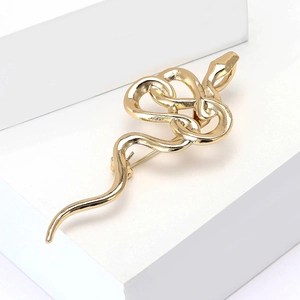 Elegant gold snake brooch with polished metallic finish on a minimalist display stand
