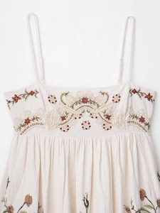 Detail of bohemian floral embroidery and smocked texture on a cream linen sundress