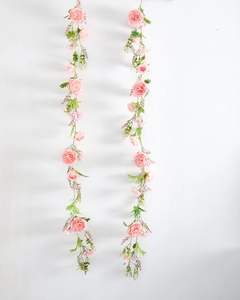 Close-up of pink artificial rose vines with realistic green leaves on a white wall