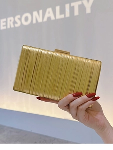 Close-up of golden clutch bag with vertical pleats held by hand against a bright background