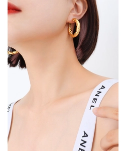 Detailed close-up of a woman wearing gold-plated twisted hoop earrings with a textured finish