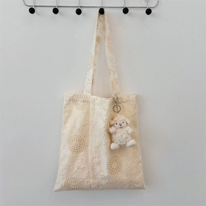 Close-up of off-white canvas tote bag with intricate floral lace embroidery and sheep charm