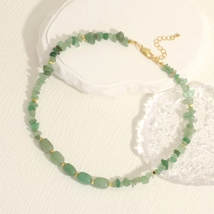 Macro detail of handmade necklace featuring green gemstone chips and gold spacers