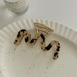 Detail of wavy tortoiseshell hair claw clip with gold metal spring on white ceramic tray