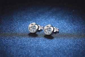 Macro shot of silver Moissanite bubble stud earrings on dark blue textured background