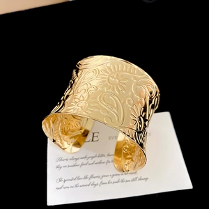 Close-up of golden wide open cuff bracelet with embossed floral and paisley textures