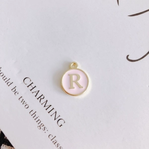 Macro shot of a pink round metal letter R pendant on a minimalist card background