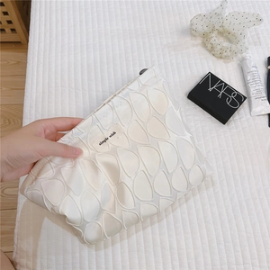 Detail of pearl white cosmetic bag with embossed floral texture and Simple Wish label