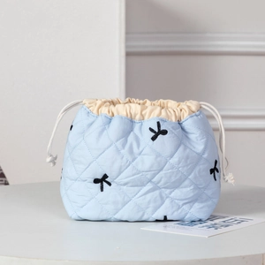 Close-up of light blue quilted drawstring bag with delicate black bow embroidery detail