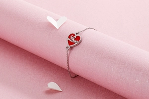 Detailed shot of a red enamel heart charm with Love script on a stainless steel bracelet