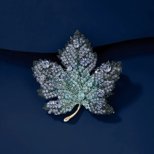 Exquisite maple leaf brooch with sparkling crystals in silver and green on blue background