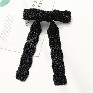 Macro detail of hand-beaded black chevron bow hair clip with long elegant tassels