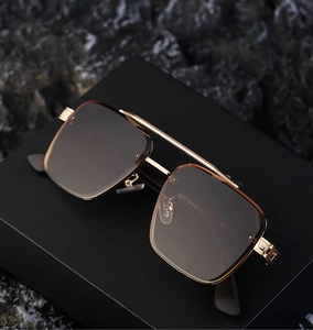 Detailed view of rectangle pilot sunglasses with gold metal frame on dark rock surface