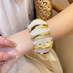 Close-up of stacked gold metal and milky white resin acrylic bracelet on model wrist