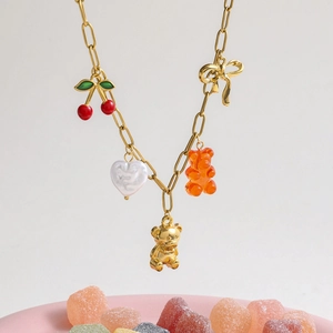 Gold metal charm bracelet with cherry bow and bear pendants over colorful candy