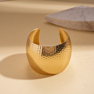 Detail of wide gold cuff bracelet featuring irregular hammered texture on beige background