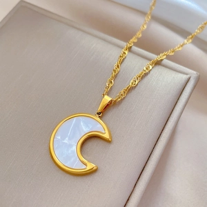 Macro shot of gold moon pendant with white shell inlay and detailed twisted chain