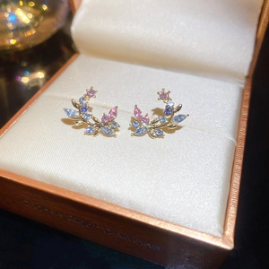 Close-up of golden branch stud earrings with blue and pink gemstones in a jewelry box