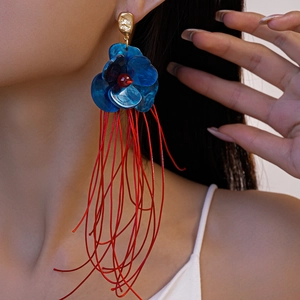 Vue latérale macro de boucles d'oreilles fleur en acrylique bleu avec franges rouges