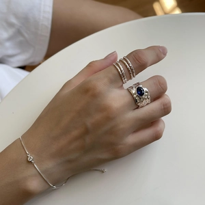 Close-up of layered silver ring and thin chain bracelet with blue gemstone on wrist