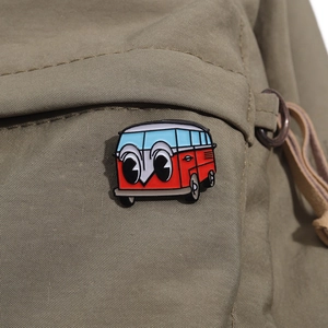 Detail einer rot-weißen Emaille-Anstecknadel im Bus-Design auf einem khakifarbenen Rucksack