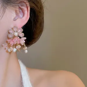 Elegant flower drop earrings with pink petals, pearls, and gold-plated tassels on a model