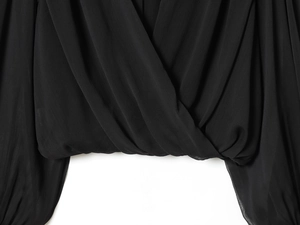 Detalle de la blusa plisada negra con textura de tela y diseño de cuello cruzado