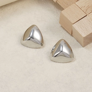 Macro view of polished silver dome triangle stud earrings on minimalist wood blocks