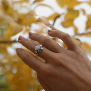 Vintage silver leaf ring with oval white opal stone on female hand with autumn background