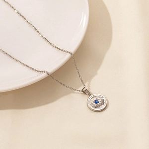 Detail of silver Evil Eye coin pendant with blue gemstone on beige textured fabric
