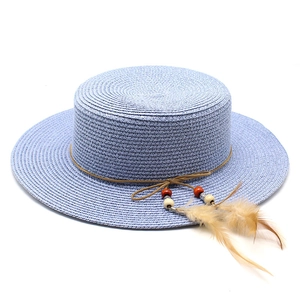 Detail of light blue flat top straw hat featuring brown cord beads and feathers