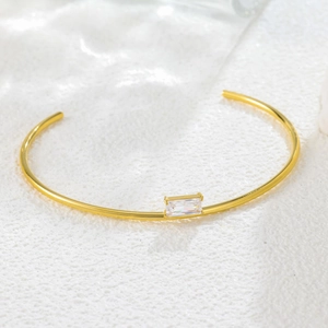 Minimalist gold cuff bracelet featuring a rectangular baguette crystal on a stone surface