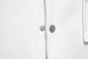 Close-up of silver-grey metal snap button on white waffle texture fabric of a men's jacket
