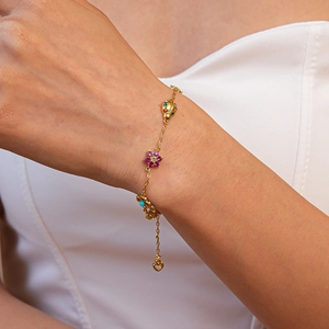 Detail of gold chain bracelet with colorful zircon ladybug and floral charms on wrist