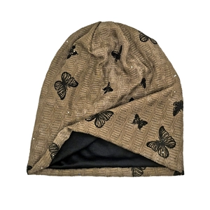 Detail of tan ribbed knit beanie featuring black butterfly embroidery and satin lining