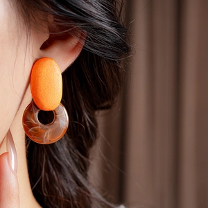 Detail of resin geometric earrings with orange oval and brown amber-textured rings