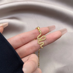 Detail of snake pendant in 18K gold plating with cubic zirconia on a gray satin background