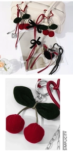 Macro detail of handmade velvet cherry charm with green leaves and black bow on heart clip