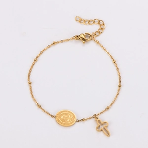Macro detail of gold stainless steel bracelet with cross charm and medallion pendant