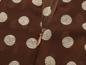 Close-up of invisible drop-shaped zipper on brown polka dot pleated chiffon fabric
