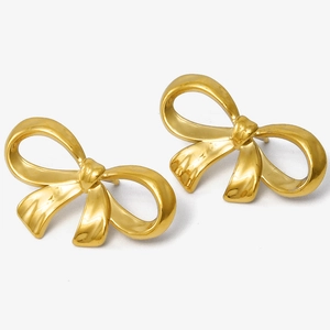 Détail des boucles d'oreilles nœud doré avec finition satinée sur un fond blanc neutre