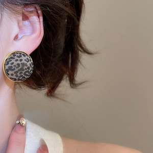 Close-up of leopard print round earring with gold metal frame worn on model's ear